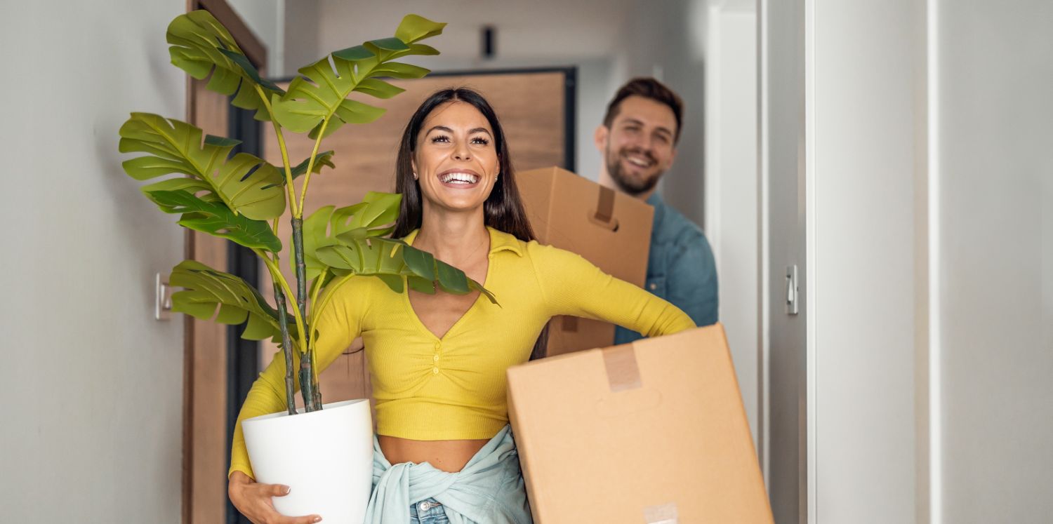 A young couple smiling carrying boxes into their new home